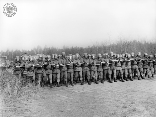 Pododdział ZOMO na ćwiczeniach na poligonie w rejonie Rzeszowa. Funkcjonariusze w tyralierze z pałkami szturmowymi trzymanymi przed sobą, wiosna 1982 roku