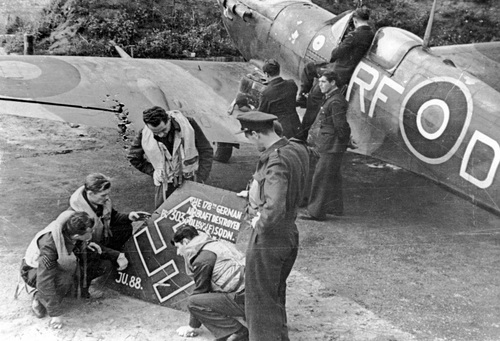 Lotnicy polskiego dywizjonu myśliwskiego 303 oglądają szczątki zestrzelonego samolotu niemieckiego „Ju 88”. Z prawej widoczny samolot „Spitfire” należący do pilota Jana Zumbacha, 1941 r. (fot. ze zbiorów NAC)