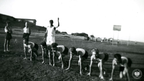 Zawodnicy przygotowujący się do biegu na 100 m, od prawej: Wiesław Stypuła, Stefan Bukowski, Marian Różański. Sygnał do startu daje Antoni Maniak. Osiedle Dzieci Polskich w Balachadi, 1945 r. (fot. z zasobu AIPN)