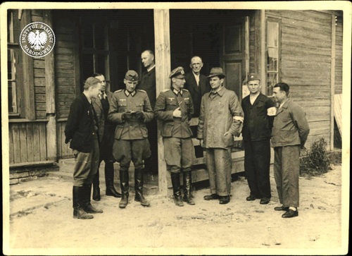 Pracownicy Komisji Technicznej PCK i niemieccy wojskowi przed drewnianym budynkiem w lesie katyńskim lub kwaterą Polaków koło stacji (przystanku) Katyń, w okresie ekshumacji, 1943 r. (fot. z zasobu AIPN)