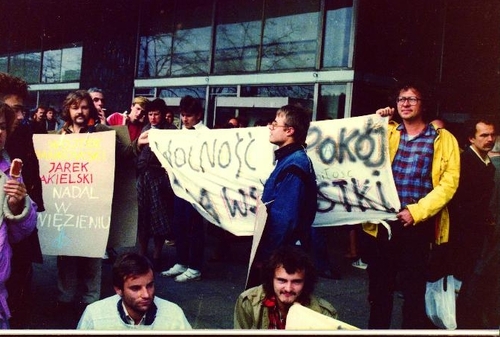 Demonstracja uliczna uczestników Ruchu „Wolność i Pokój" przed Domami Towarowymi „Centrum" w Warszawie, 3 października 1986 roku; po lewej Marek Adamkiewicz, po prawej Wojciech Bafeltowski, Jerzy Kolarzowski, transparent trzymają Roland Kruk (po lewej) i Jarema Dubiel (fot. ze zbiorów M. Adamkiewicza)